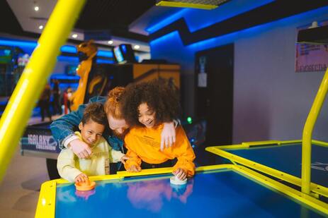 2 children and adult playing air hockey at the arcade 